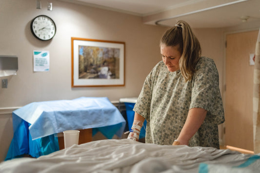 Pregnant woman in a gray and white floral shirt sitting on the bed.